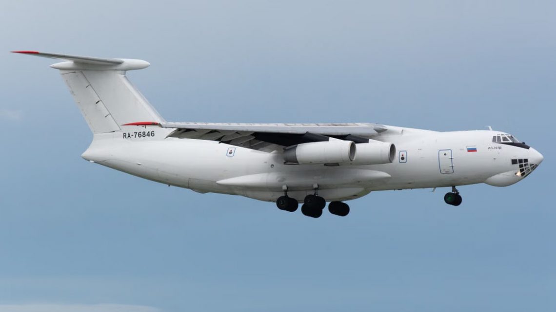 White IL-76 cargo aircraft with visible markings flying against a clear sky.