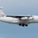 White IL-76 cargo aircraft with visible markings flying against a clear sky.